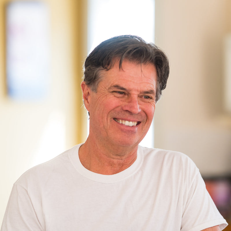 Image of Tim, owner of Tim's Serious Shake, wearing a white t-shirt in an blurred indoor setting and smiling