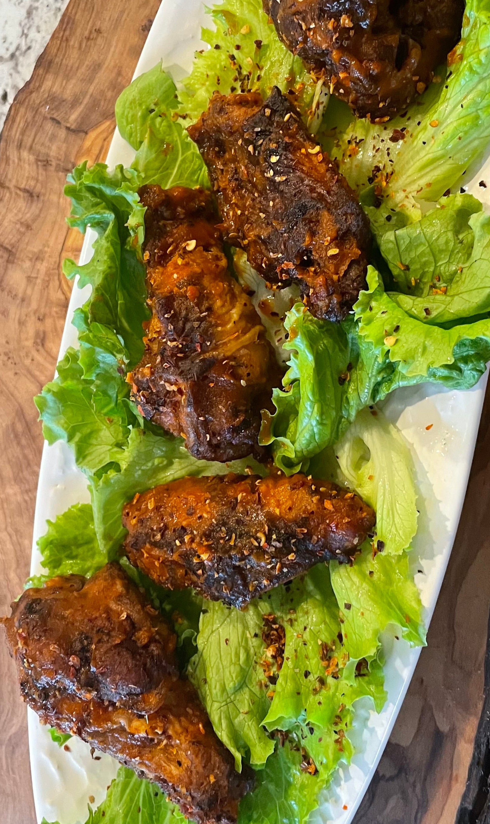 Platter of roasted chicken wings on a bed of lettuce with a wooden cutting board background